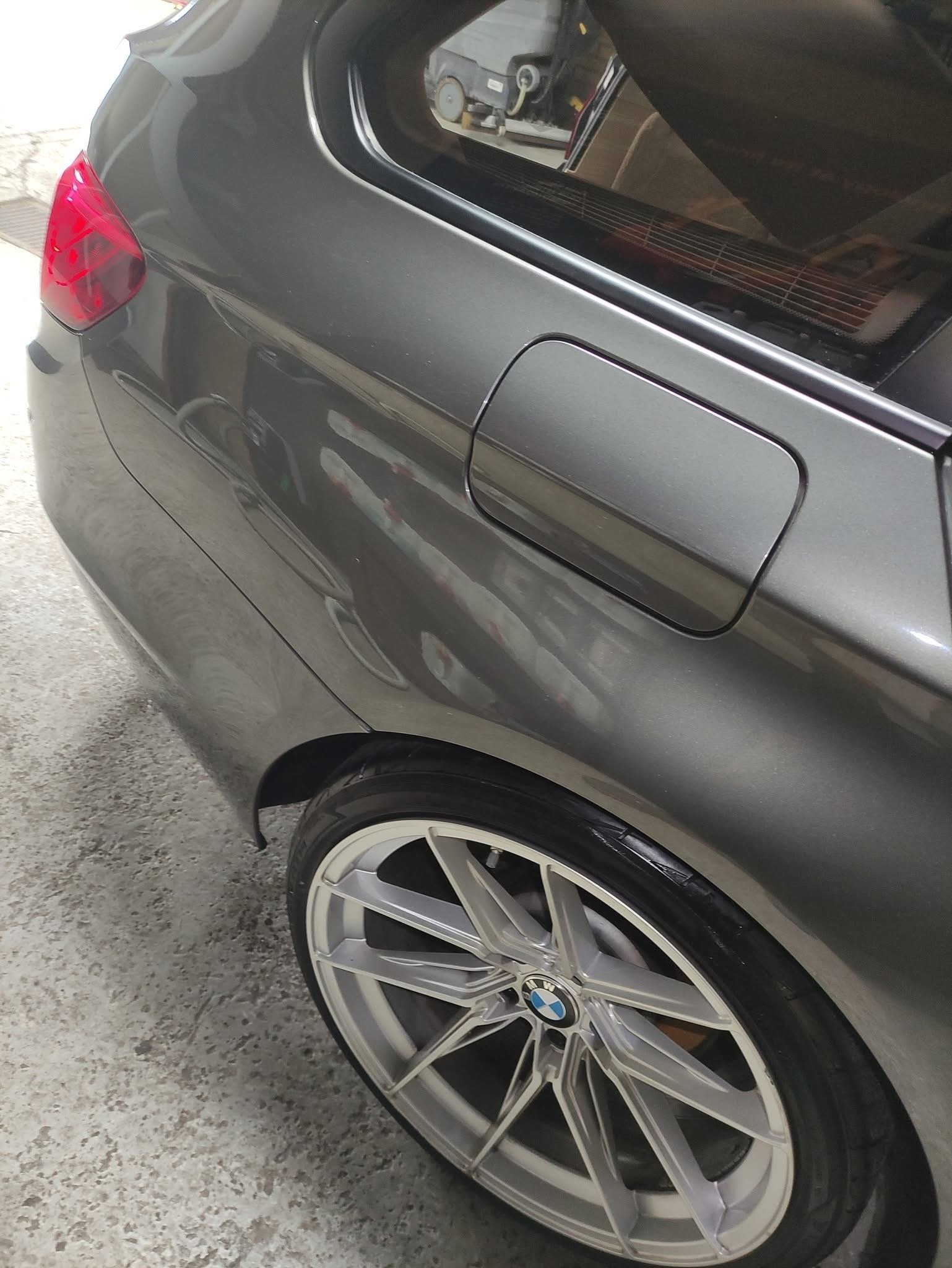 Close-up of silver cars rear side showing fuel door, red taillight, and alloy wheel on pavement