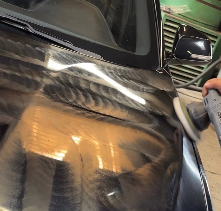 Close-up of vehicle hood showing damage with person holding spray bottle for repair or detailing